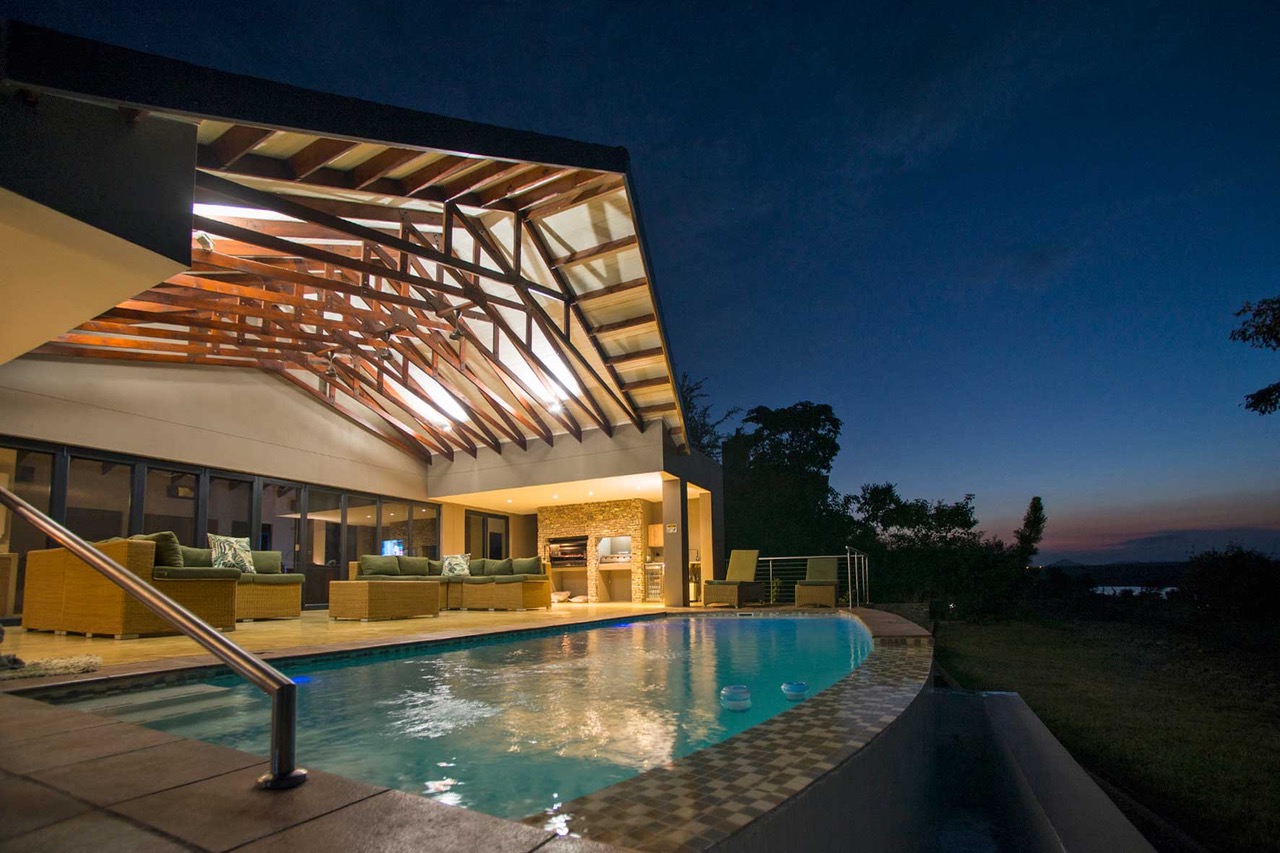 Lodge exterior at dusk with pool and stoep illuminated